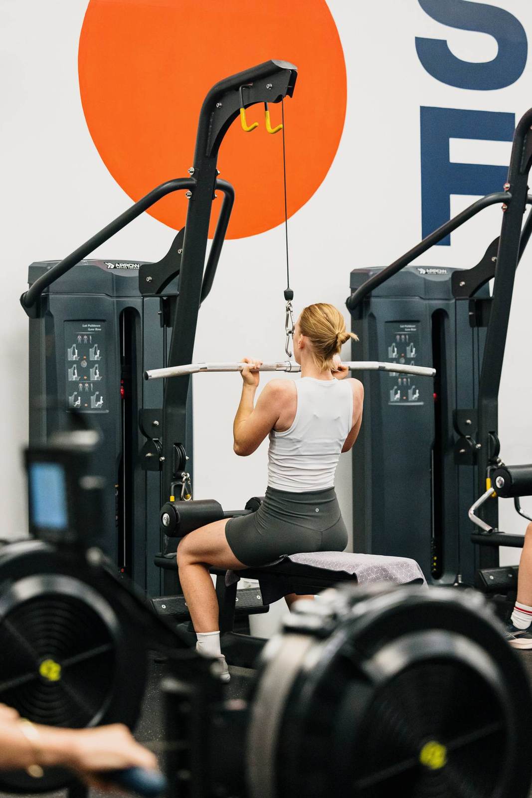 A member trains on the lat pulldown in front of the Sunrise Fitness sun mural